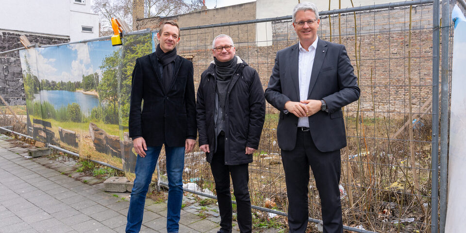 Stadtrat Valerius, gewobau-Geschäftsführer Regenstein und Oberbürgermeister Burghardt vor der Fläche der Brandruine