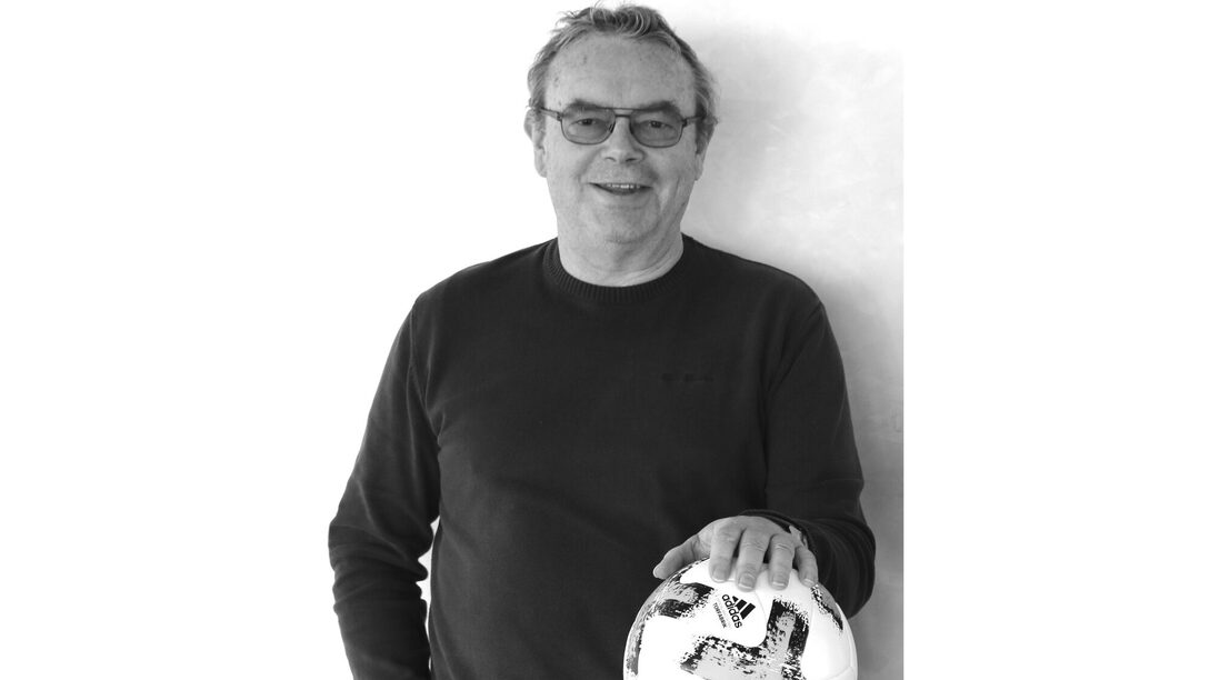 Schwarz-weißes Foto von Robert Neubauer, dessen linke Hand auf einem Fußball auf dem Tisch vor sich liegt.