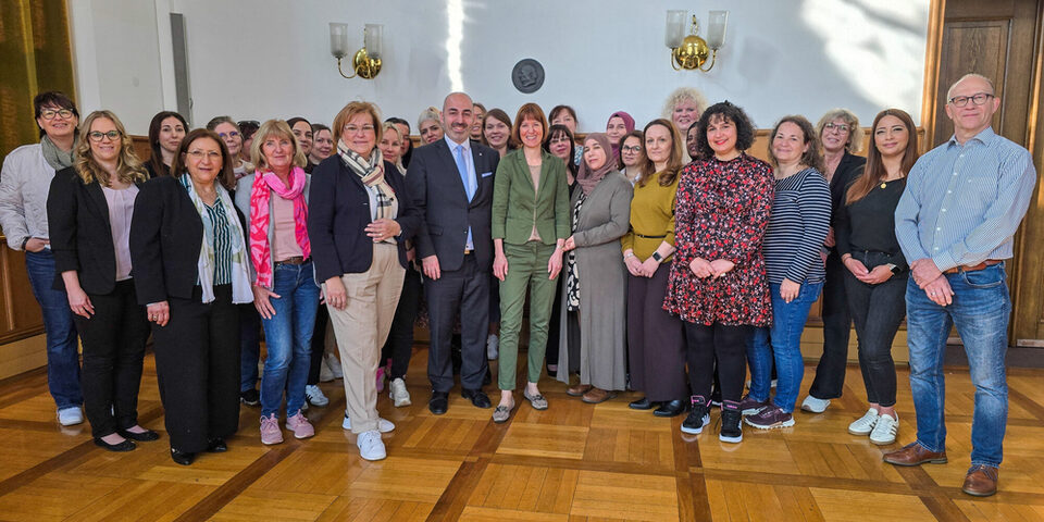 Viele Personen stehen vor einer weißen Wand und schauen in Richtung Kamera.