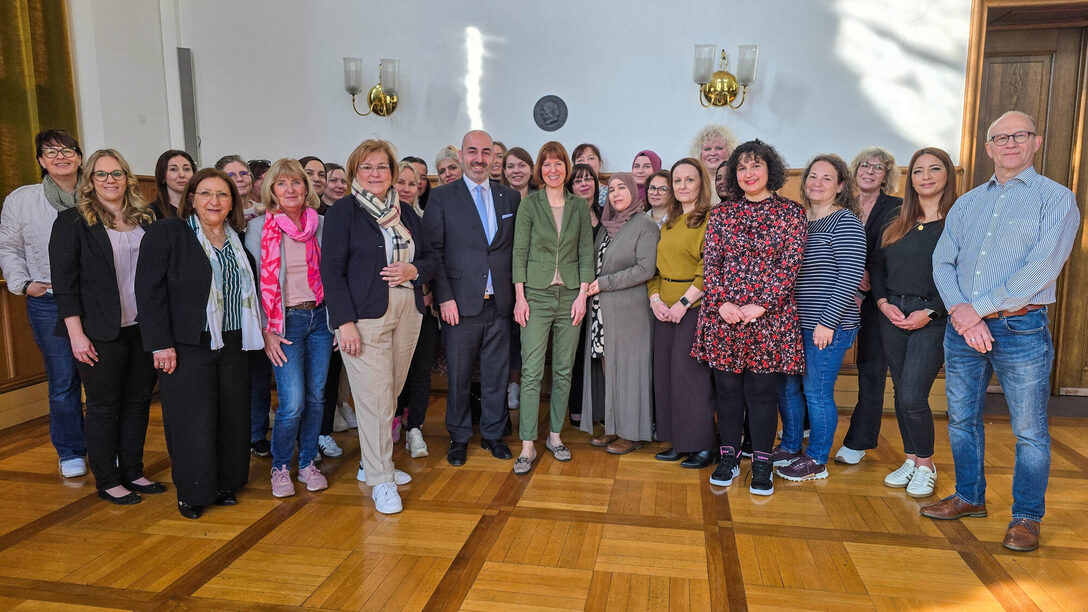 Viele Personen stehen vor einer weißen Wand und schauen in Richtung Kamera.