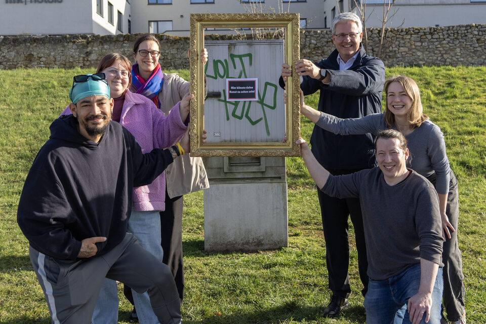 Projektbeteiligte halten einen Bilderrahmen vor einen Stromkasten