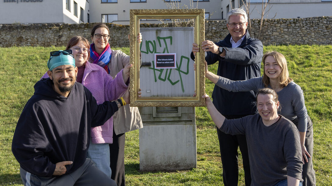 Projektbeteiligte halten einen Bilderrahmen vor einen Stromkasten