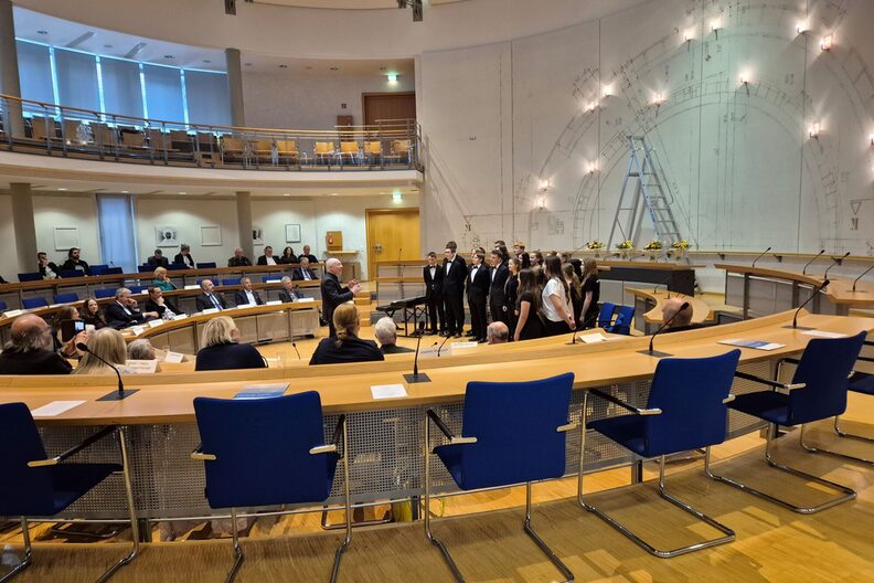 Ratssaal mit Gästen, Chor und der Kunstinstallation im Hintergrund.