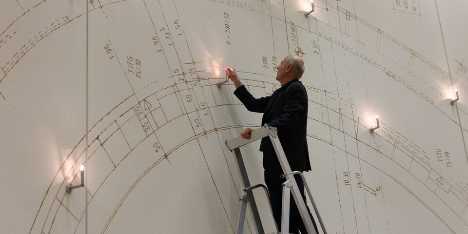 Vollrad Kutscher steht auf einer Leiter und installiert das Porträt im Kunstwerk.