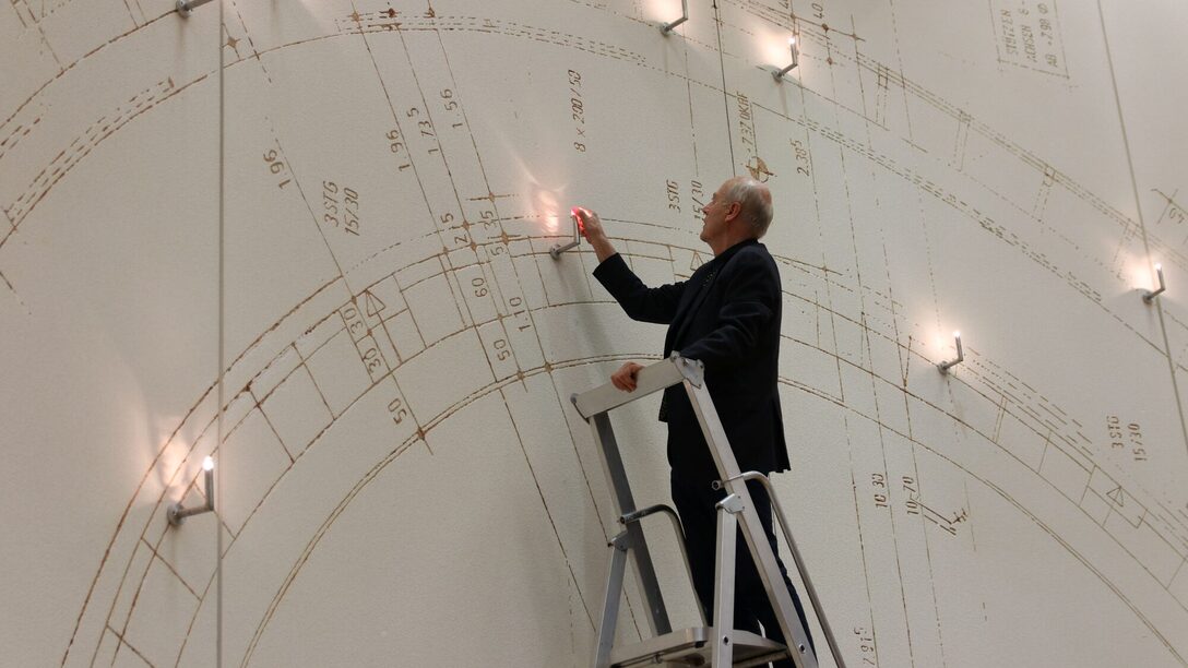 Vollrad Kutscher steht auf einer Leiter und installiert das Porträt im Kunstwerk.