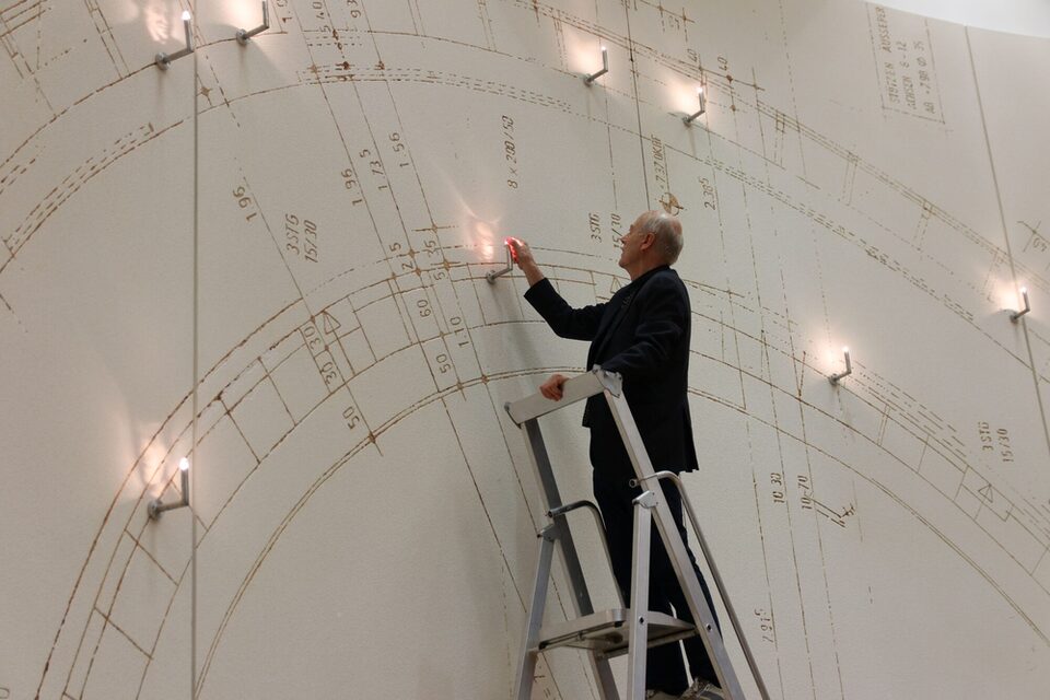 Vollrad Kutscher steht auf einer Leiter und installiert das Porträt im Kunstwerk.