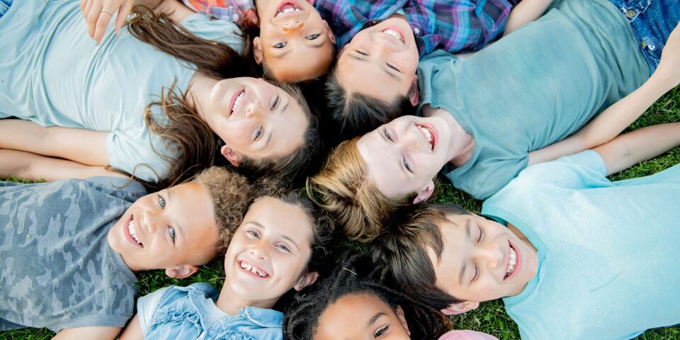 lachende Kinder liegen im Kreis auf einer Wiese