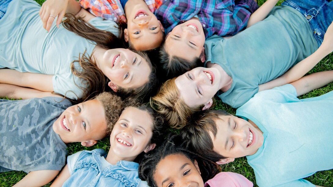 lachende Kinder liegen im Kreis auf einer Wiese