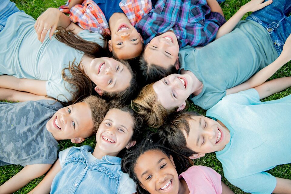 lachende Kinder liegen im Kreis auf einer Wiese