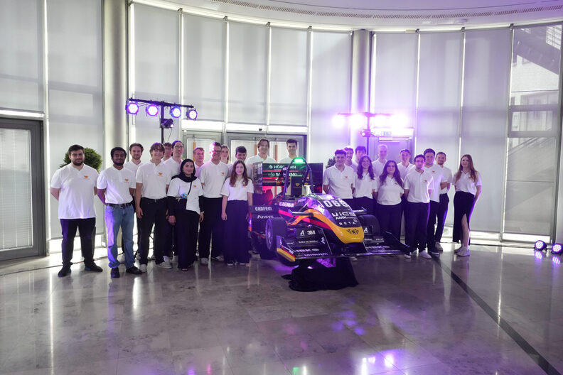 25 Mitglieder des Scuderia Mensa Teams stehen neben dem Rennwagen.