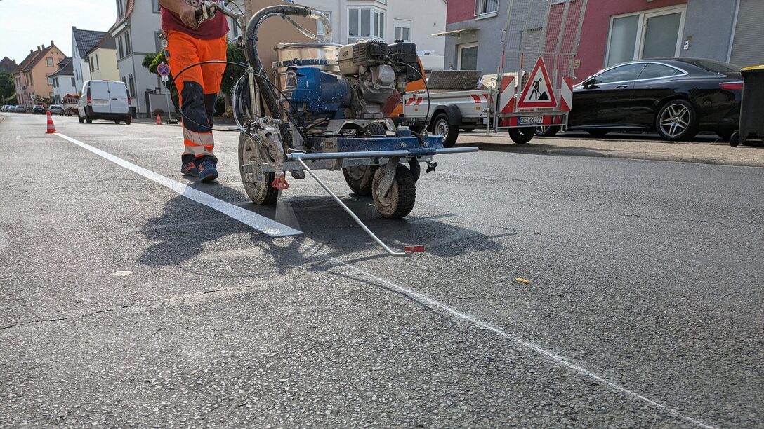 Mit einer Maschine wird auf dem Asphalt weiße Farbe für die Parkmarkierung aufgetragen.