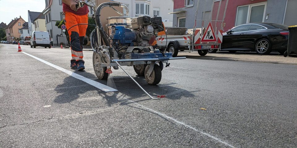Mit einer Maschine wird auf dem Asphalt weiße Farbe für die Parkmarkierung aufgetragen.