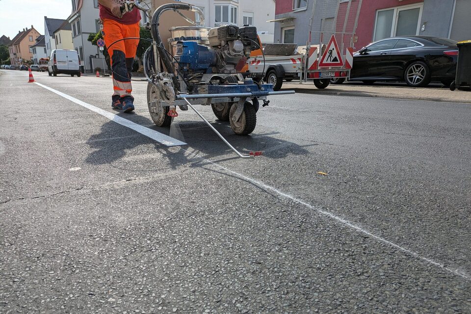 Mit einer Maschine wird auf dem Asphalt weiße Farbe für die Parkmarkierung aufgetragen.