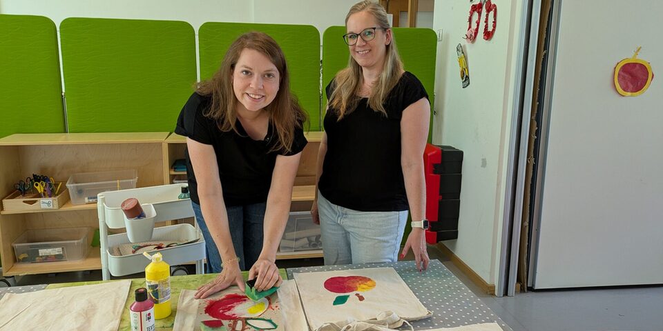 Kita-Assistenz bedruckt Stofftaschen, neben ihr steht die Kita-Leiterin