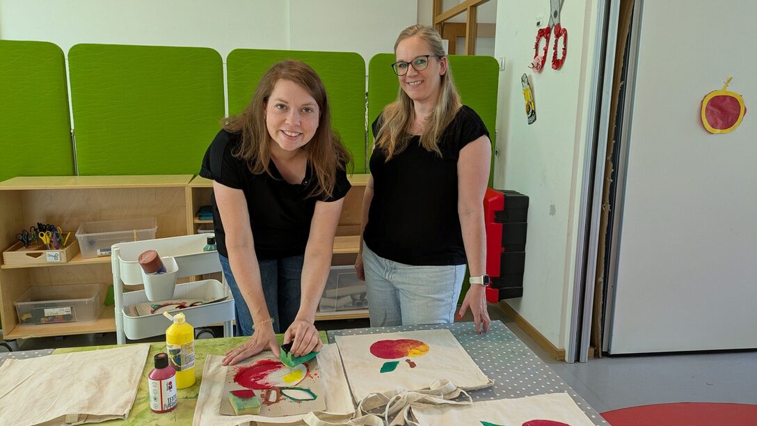 Kita-Assistenz bedruckt Stofftaschen, neben ihr steht die Kita-Leiterin