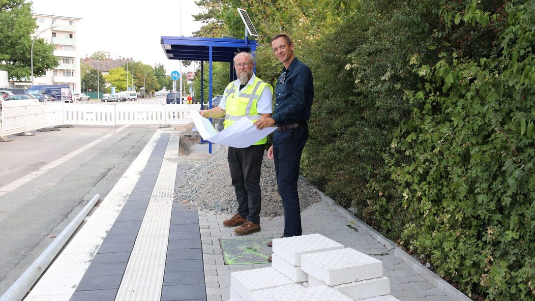 Stadtrat und Abteilungsleiter sehen sich auf der Baustelle für die Haltestelle an der Alexander-von-Humboldt-Schule einen Bauplan an.