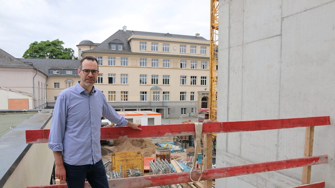 Stadtrat Nils Kraft steht vor der Baustelle Parkschule. Im Hintergrund ist das alte Hauptgebäude zu sehen.