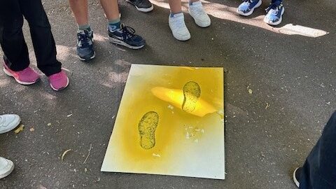 Eine Schülergruppe umkreist die Asphaltmarkierung Gelbe-Füße