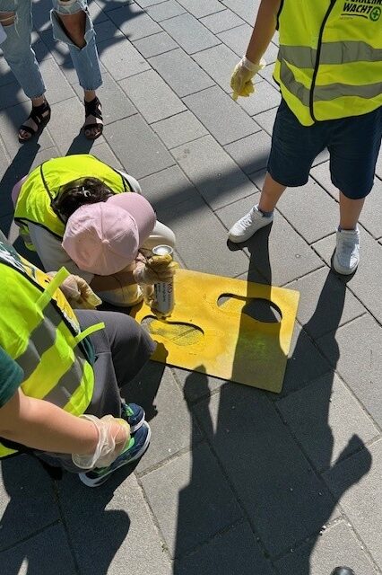 Schüler sprayen die Markierung 'Gelbe-Füße' auf den Asphalt
