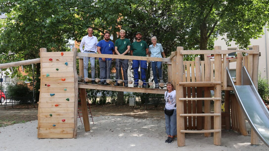 Spielplatz Liebigstraße, Auf dem Steg seht Stadtrat Simon Valerius mit Mitarbeitenden der Spielplatzcrew des Städteservices. Unten steht Frau Beate Bopp von der städtischen Grünplanung.