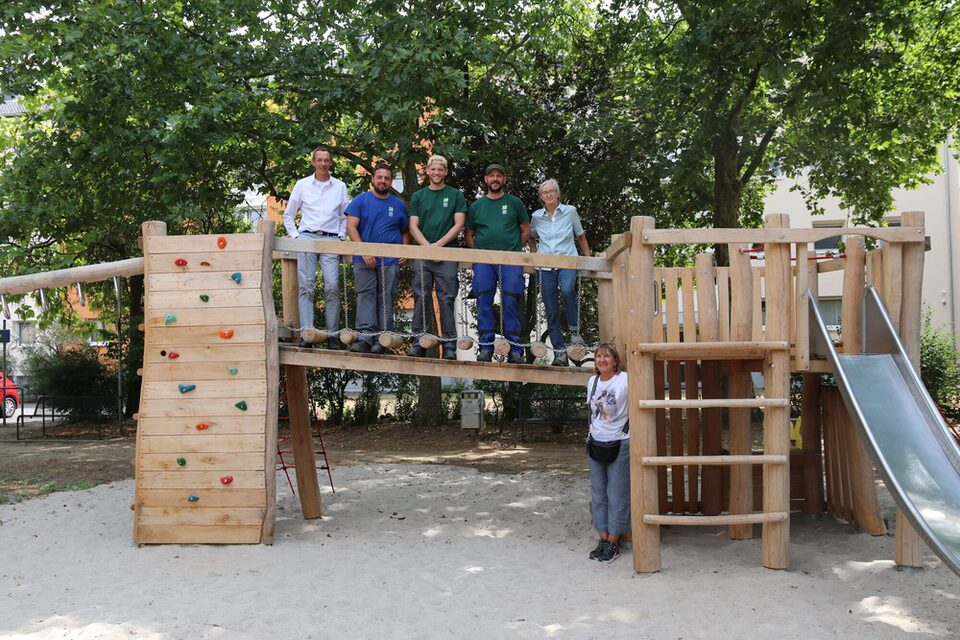 Spielplatz Liebigstraße, Auf dem Steg seht Stadtrat Simon Valerius mit Mitarbeitenden der Spielplatzcrew des Städteservices. Unten steht Frau Beate Bopp von der städtischen Grünplanung.