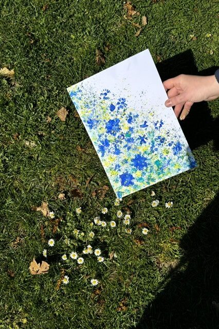 Eine Hand hälz ein mit Blumen bemaltes Blatt