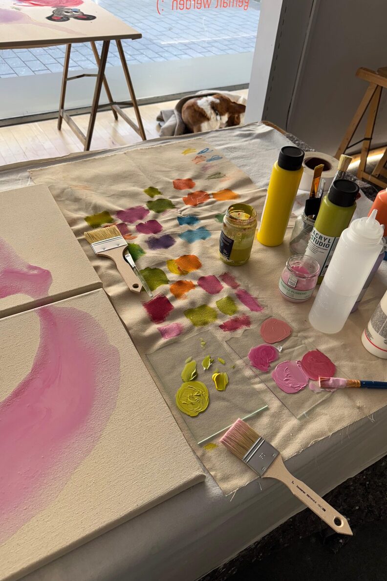 Farbmischung von Rosa- und Gelbtönen, links ist eine Leinwand zu sehen, im Vordergrund ein Pinsel