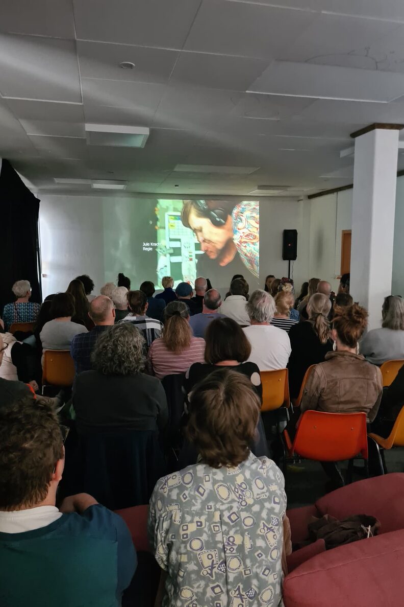 Zuschauerinnen und Zuschauer sitzen im freiraum f3 und schauen einem Vortrag auf einer Leinwand zu