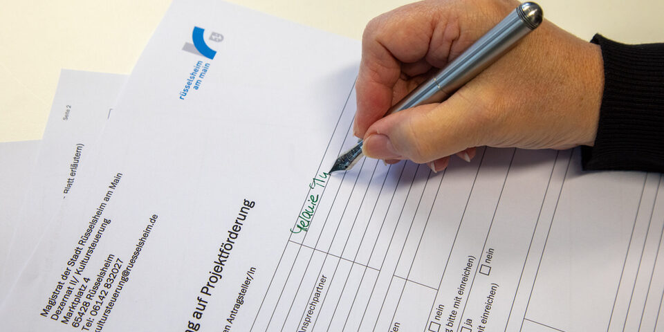 Hand hält einen Stift und füllt den Antrag zur Projektförderung aus