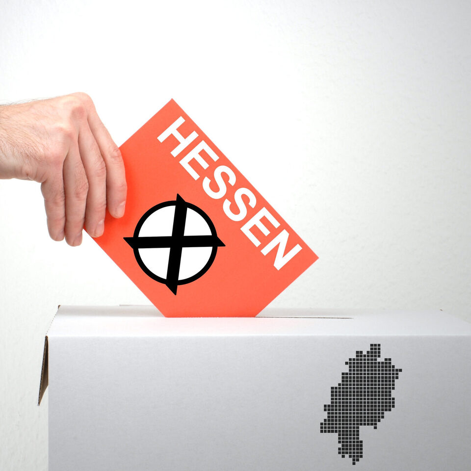 Eine Hand hält eine Karte mit dem angekreuzten Aufdruck "Hessen" über eine Wahlurne