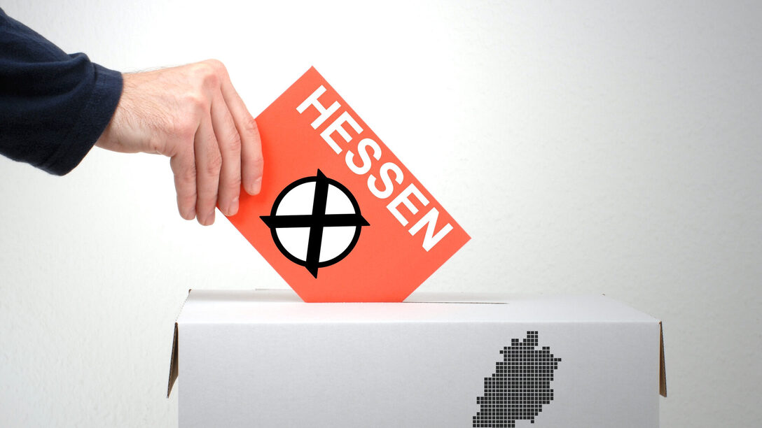 Eine Hand hält eine Karte mit dem angekreuzten Aufdruck "Hessen" über eine Wahlurne