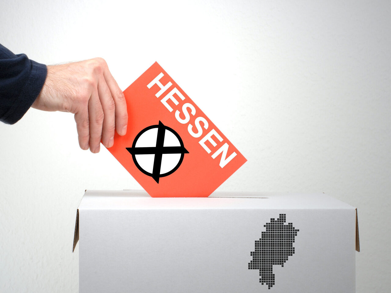 Eine Hand hält eine Karte mit dem angekreuzten Aufdruck "Hessen" über eine Wahlurne