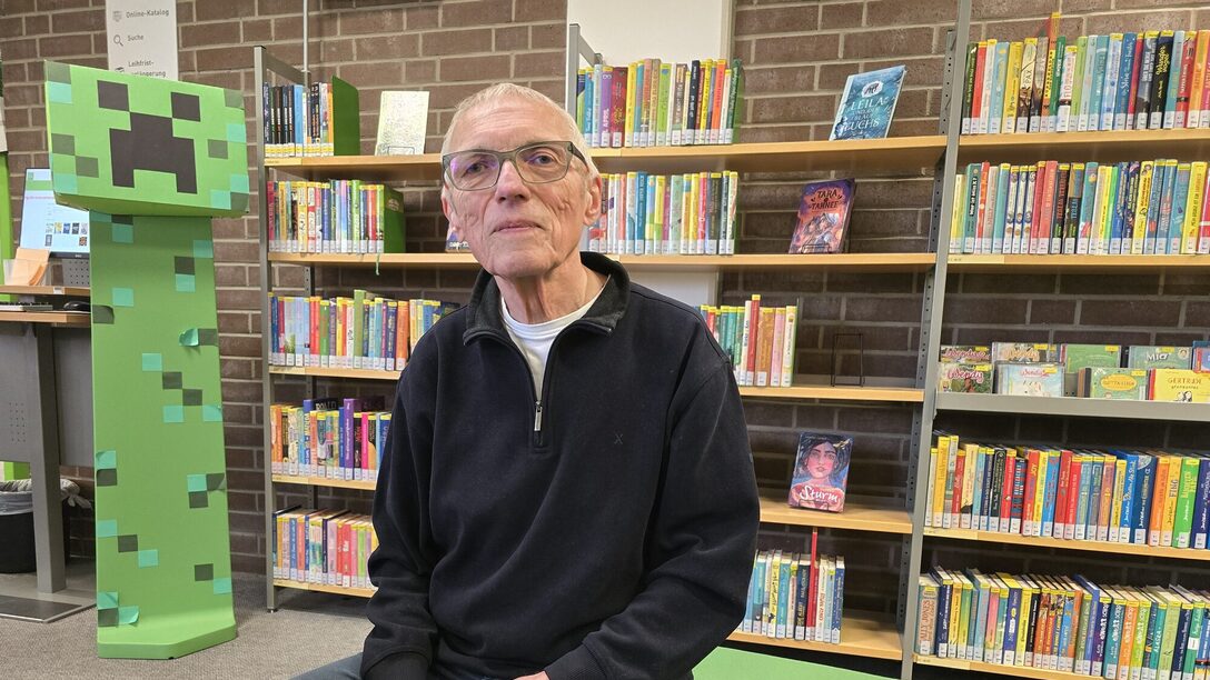 Egon Christ sitzt in der Stadtbücherei vor einem Bücherregal