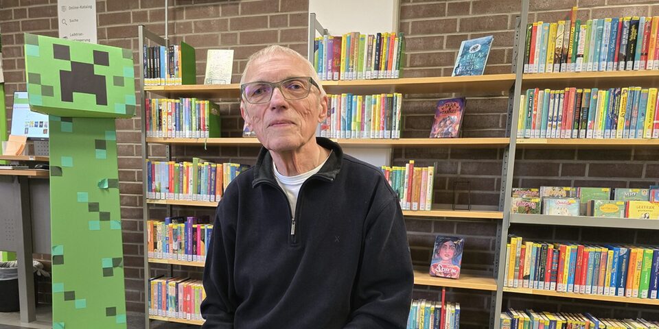 Egon Christ sitzt in der Stadtbücherei vor einem Bücherregal
