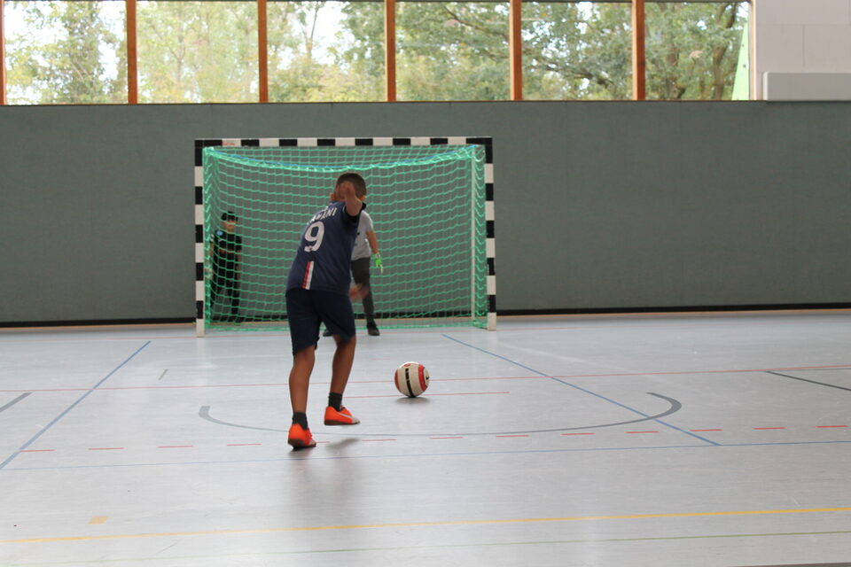 Eine Fußballspielerin mit Ball vor dem Tor in einer Sporthalle