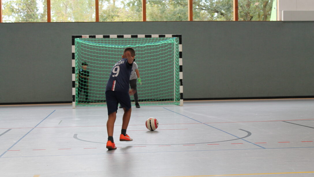 Eine Fußballspielerin mit Ball vor dem Tor in einer Sporthalle