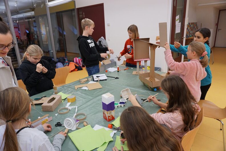 Eine Gruppe Kinder steht und sitzt an einem Tisch und bastelt etwas