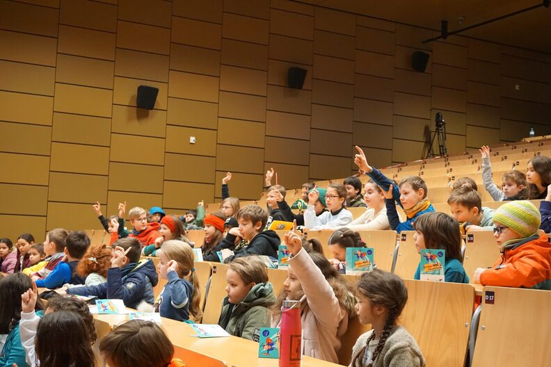Kinder sitzen in einem Hörsaal, einige melden sich