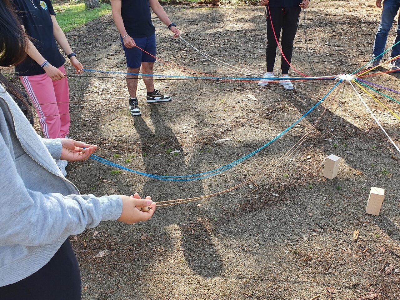 Jugendliche halten bunte Schnüre in den Händen, mit denen sie einen Holzklotz anheben.