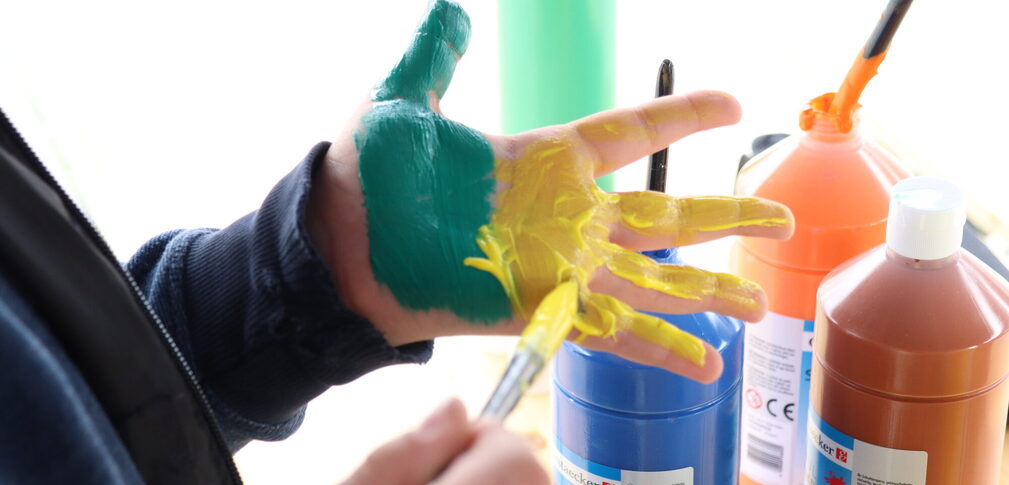 Ein Junge bemalt seine Hand mit gelber und grüner Farbe um einen Abdruck zu machen.