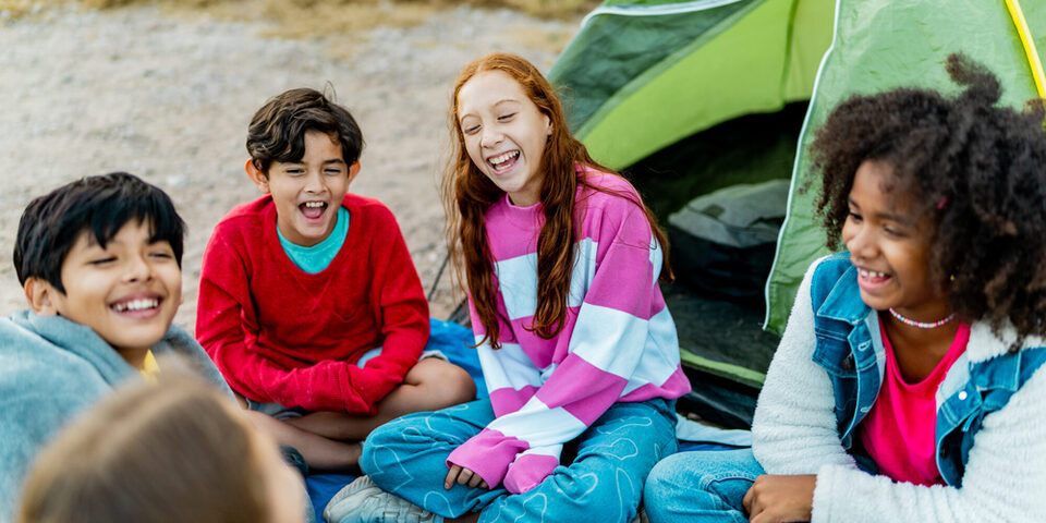 Kinder sitzen vor einem Zelt und lachen