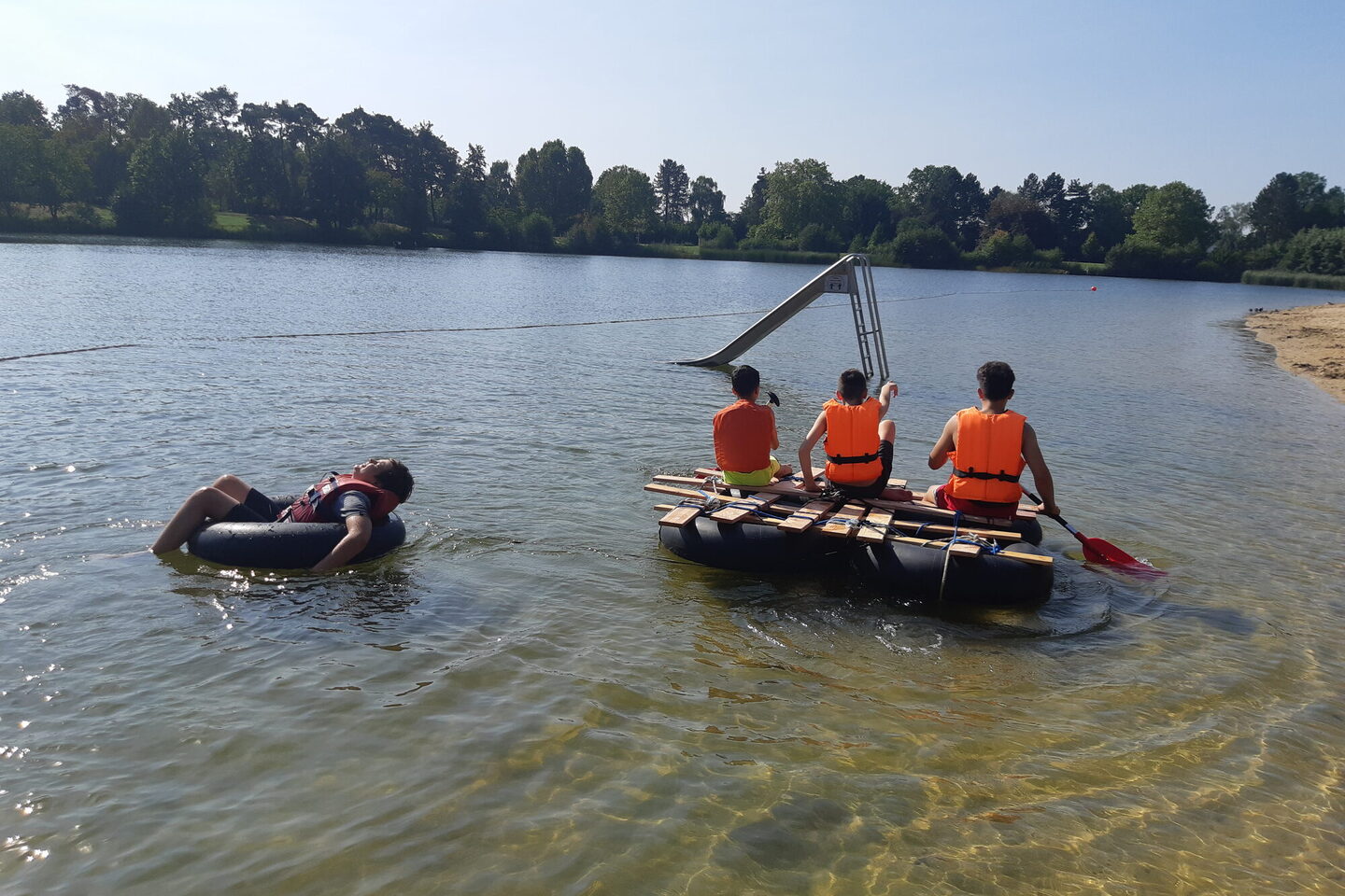 Jugendliche fahren auf einem selbstgebauten Floß auf dem Badesee