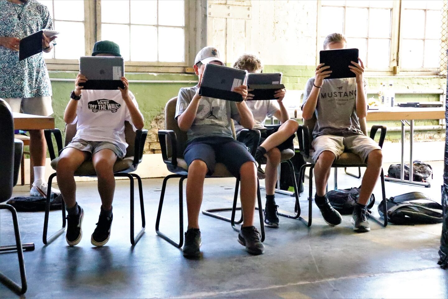Jugendliche sitzen auf Stülen und blicken vertieft auf ein Tablet.