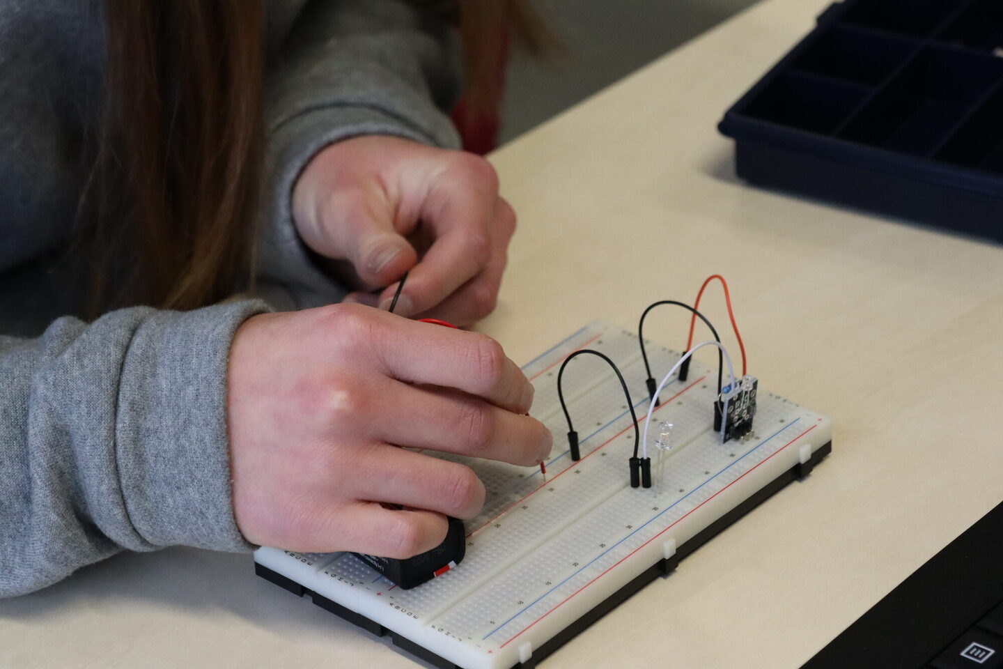 Eine Jugendliche steckt auf einer Platine verschiedene Kabel zusammen.