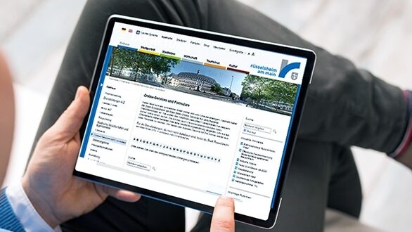 Zwei Hände halten ein Tablet, auf dem ein Online-Service der Stadt Rüsselsheim zu sehen ist.