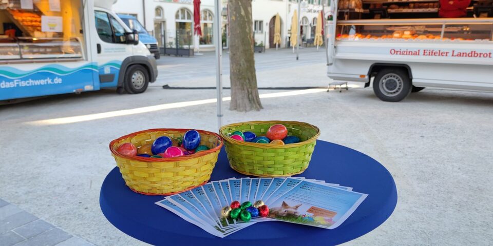 Kürbe mit Ostereiern auf einem Tisch bei der Osteraktion, im Vordergrud liegen Infoblätter und Schokoladeneier auf dem Tisch