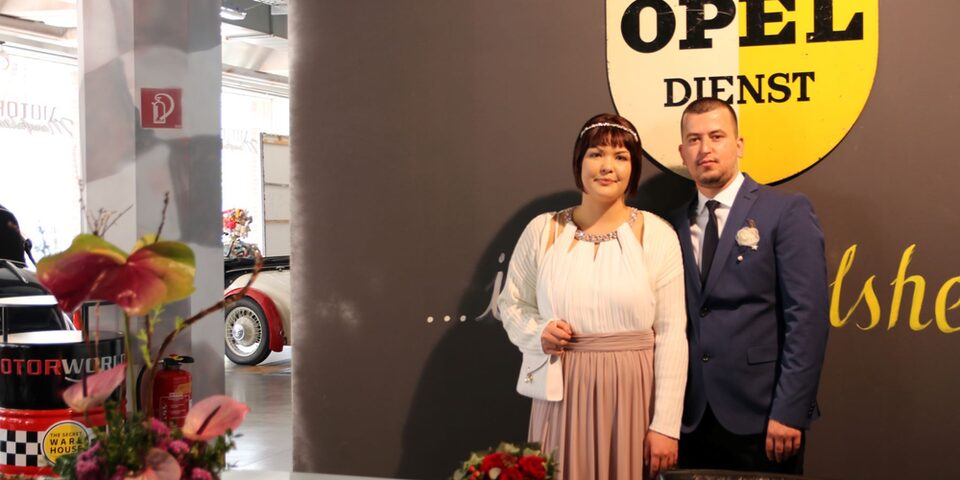 Diana und Kledjus vor einem historischen Opel-Emblem in der MOTORWORLD