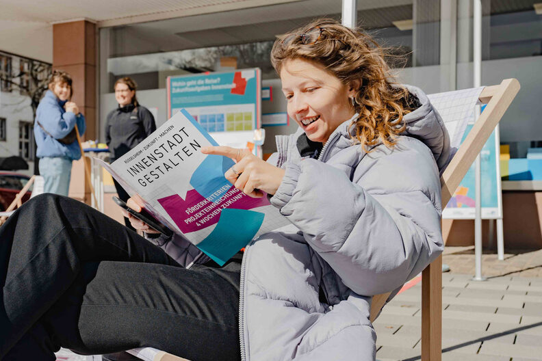Junge Frau sitzt in einem Stuhl und schaut sich eine Broschüre an
